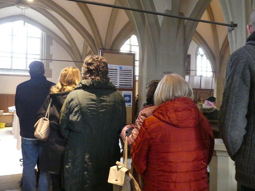 Mehrere Menschen stehen in der Kirche in einer Schlange, von hinten aufgenommen