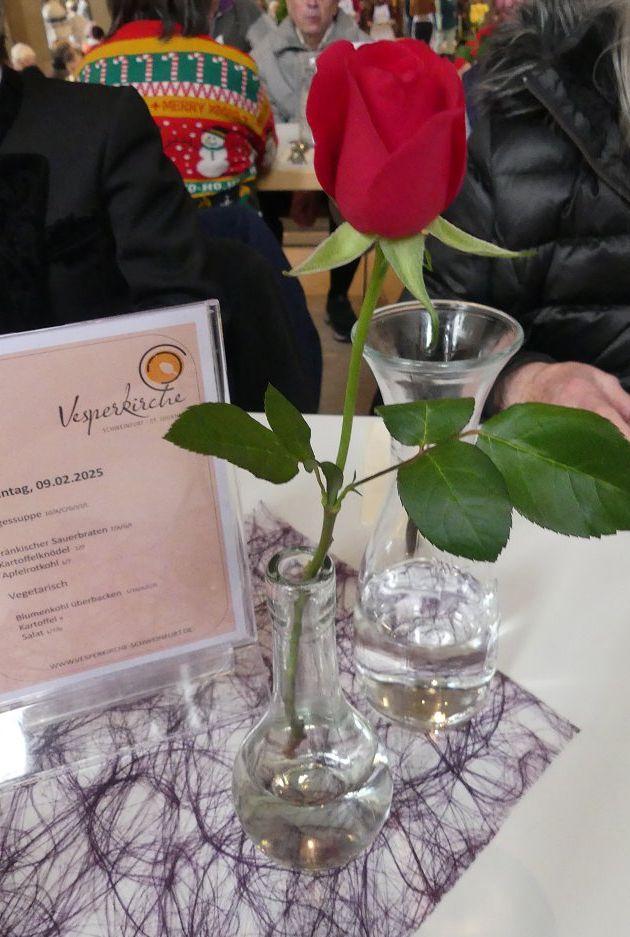 Ein Aufsteller mit dem Menü des Tages, eine Wasserkaraffe, eine Vase mit einer Rose.